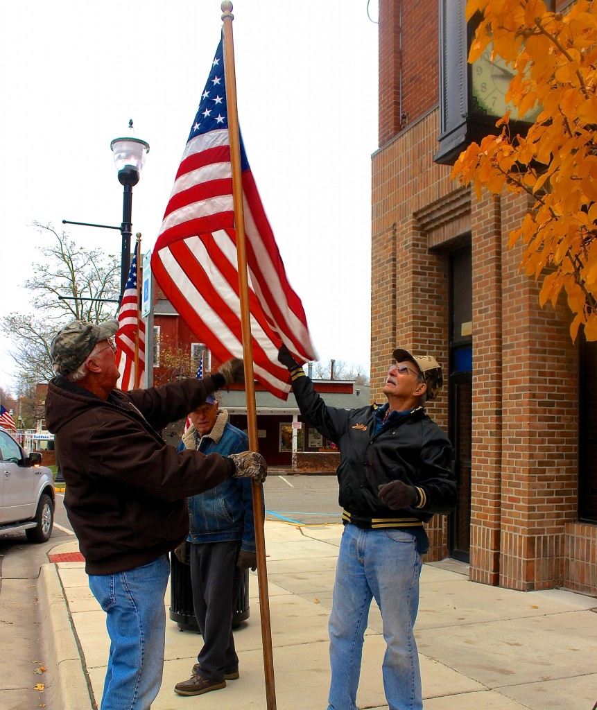 Men from Manchester's American Legion Post 117 debate the proper position of a flag planted in front of the Comerica Bank on Main Street.
