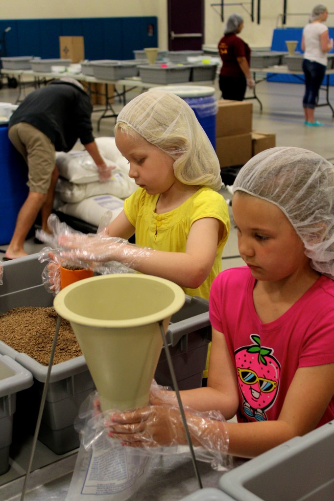 Mallory Klein (in pink) holds the meal bag under the funnel as Hayleigh Weatherholt (in yellow) prepares a scoop of soy.