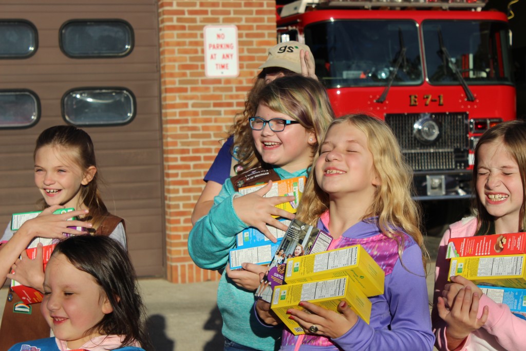 Girl Scouts squinting into the setting sun outside the Fire Department's monthly meeting before presenting firefighters with Girl Scout cookies.