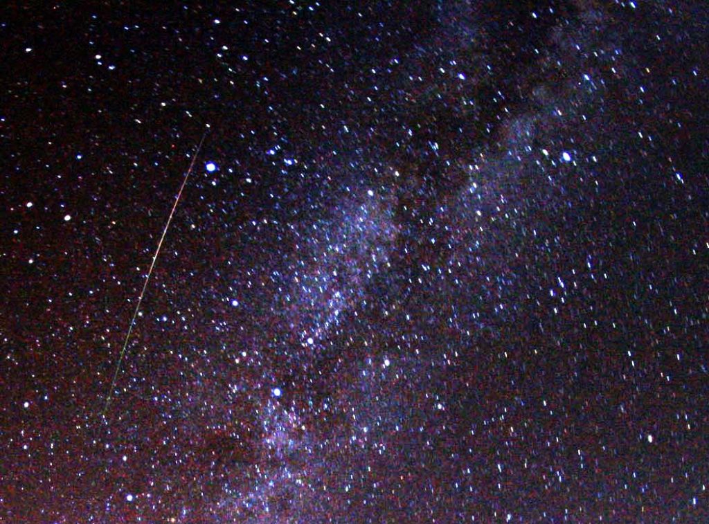 A multicolored, long Perseid meteor striking the sky just to the left of Milky Way.